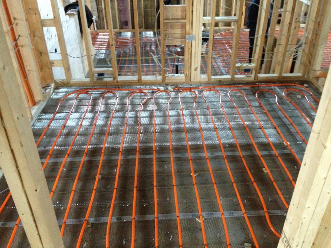 Red and blue floor heating tubes installed in a rectangular pattern within a wooden‑framed room.