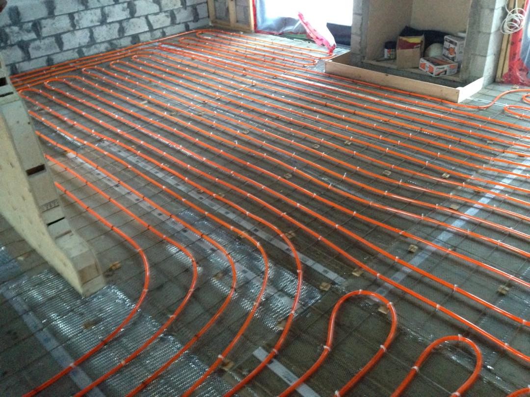 Curved red and blue heating tubes laid evenly across a floor surface inside a building under construction.