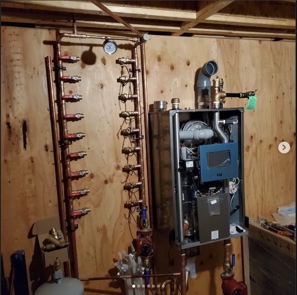 Wall-mounted mechanical panel with copper pipes, valves, and control components arranged vertically in a utility room.